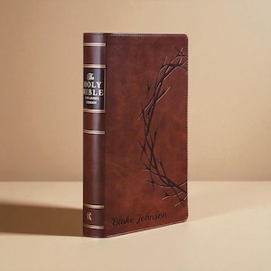 May include: A brown leather-bound Bible with gold lettering and accents. The spine reads "The Holy Bible, King James Version." A crown of thorns design is embossed on the cover, with the name "Blake Johnson" at the bottom.
