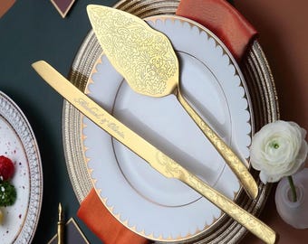 以下が含まれることがあります： 金色のケーキナイフとサーバーのセット。華やかなフローラルパターンが施されています。「Michael & Olivia」の名前が刻印されています。 金色の縁取りのある白いお皿の上に置かれています。