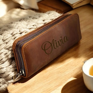May include: A brown leather pencil case with a zipper closure. The case is personalized with the name "Olivia" in a cursive font.
