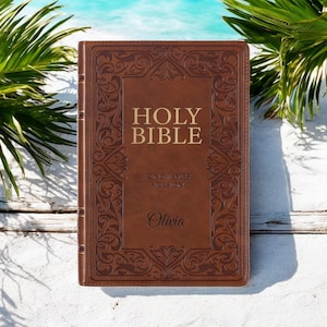 May include: A brown leather-bound Holy Bible with gold lettering and an ornate design. The Bible is personalised with the name "Olivia" and features the King James Version.
