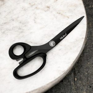 Puede incluir: Tijeras de tela negras con un tornillo plateado y el nombre "Michael" grabado en la hoja.