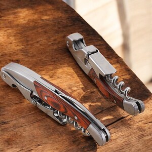 May include: Two silver and wood wine bottle openers with a corkscrew and a foil cutter. The openers have a wood handle with a red and brown wood grain pattern.