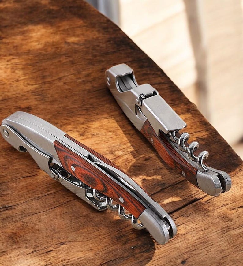 May include: Two silver and wood wine bottle openers with a corkscrew and a foil cutter. The openers have a wood handle with a red and brown wood grain pattern.