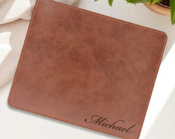 May include: A rectangular brown leather mousepad with stitched edges. The name "Michael" is elegantly engraved in a cursive font on the lower right corner. The mousepad is a solid color and has a smooth texture.