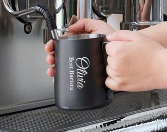May include: A black stainless steel milk frothing pitcher with a white inscription that reads "Olivia Best Barista".