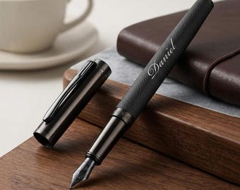 May include: A black fountain pen with a textured grip and a metallic finish, featuring the name Daniel engraved in a cursive script on the barrel. The pen is shown with its matching cap removed, revealing a detailed silver-toned metal nib.