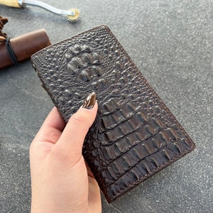 May include: A brown leather wallet with a crocodile pattern. The wallet is closed and has a flap.