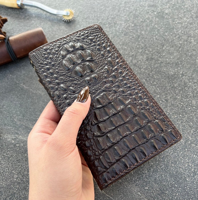 May include: A brown leather wallet with a crocodile pattern. The wallet is closed and has a flap.