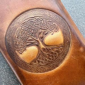 May include: A brown leather wallet with a Celtic knot design featuring a tree of life motif.