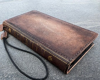 May include: A brown leather phone case with a vintage book design. The case has a black strap and gold accents.