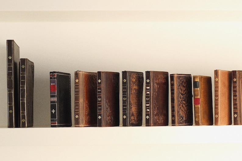 May include: A collection of antique books with leather-bound covers, arranged on a shelf. The books vary in color from dark brown to tan, with some featuring decorative gold accents and red or black spines. The spines are visible, showcasing titles and details.