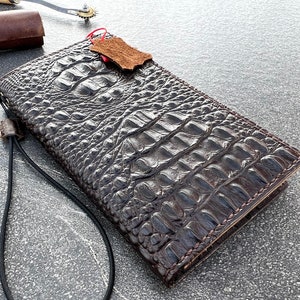 May include: A dark brown alligator skin wallet with a strap. The wallet has a textured surface and is made of high-quality leather.