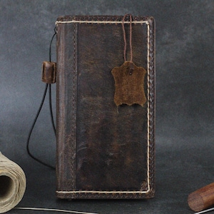 May include: A brown leather wallet with a white stitching detail and a small leather tag. The wallet has a strap and is closed.
