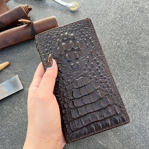 May include: A brown leather wallet with a crocodile embossed pattern. The wallet is closed and has a smooth, glossy finish.