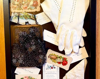 May include: A framed display with vintage ephemera, including a beaded purse, white gloves, and several cards with floral and bird motifs. The cards include text such as "With love and pleasant wishes dear," and "Miss Irene O'Donnell."