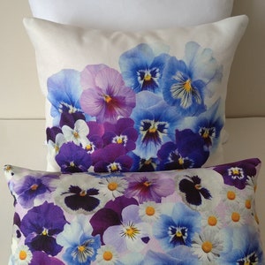 May include: Three decorative pillows. The top pillow is plain white. The middle pillow features a print of blue and purple pansies. The bottom pillow has a print of pansies and daisies in shades of purple, blue, and white.