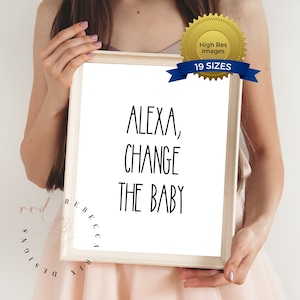 May include: A framed print with the text "ALEXA, CHANGE THE BABY" in black, sans-serif font. The print is held by a person. The frame is light-colored wood. A gold seal with the text "High Res Images" and a blue banner with "19 SIZES" are in the upper right corner.