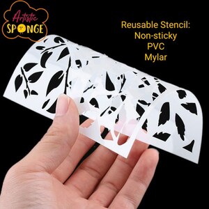 Puede incluir: Plantilla reutilizable blanca con un dise&ntilde;o de hojas. La plantilla est&aacute; hecha de PVC Mylar no pegajoso. La plantilla est&aacute; siendo sostenida por una mano.