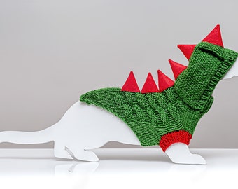 May include: Green knitted dog sweater with a red hooded dinosaur design. The sweater has red felt spikes on the back and red felt trim on the sleeves.