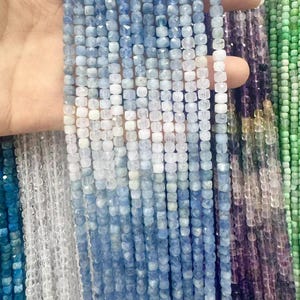 May include: A strand of light blue, medium blue, and dark blue faceted square beads. The beads are strung on a clear thread. The beads are all the same size and shape.