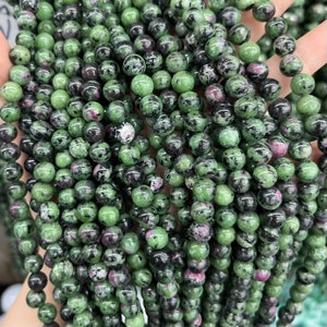 以下が含まれることがあります： 緑、黒、ピンクの宝石ビーズのストランド。ビーズは丸く、斑点模様です。