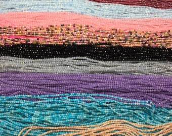 May include: A collection of various colored gemstone beads, including pink, blue, purple, turquoise, and black. The beads are arranged in rows, creating a colorful and textured pattern.