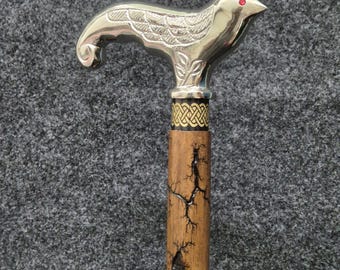 May include: A silver-colored walking cane with a bird-shaped handle. The bird has red eyes and detailed wing and feather engravings. The wooden shaft has a unique, cracked pattern. The cane's handle is 3.5 inches wide.
