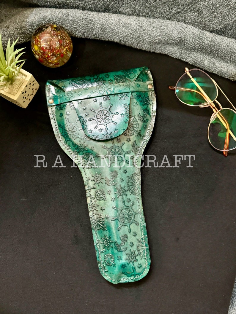 Puede incluir: Un estuche para gafas de cuero verde con tem&aacute;tica n&aacute;utica. El estuche est&aacute; decorado con anclas, estrellas y timones de barco. El estuche tiene una solapa con cierre de presi&oacute;n.