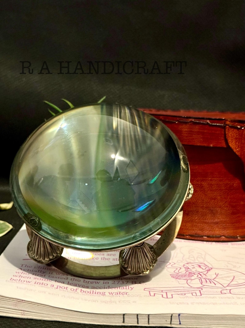May include: A silver-colored magnifying glass with a round, clear glass lens. The lens is reflecting a green and blue pattern. The magnifying glass is sitting on a book with text.