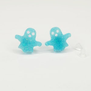 May include: A pair of blue glitter ghost stud earrings with white eyes. The earrings come with clear silicone backs.