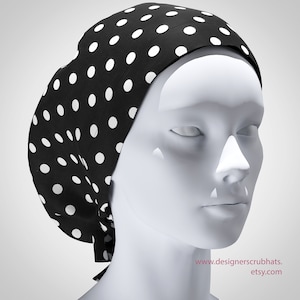 Op de afbeelding: Een zwarte scrubmuts met een witte polka dot patroon. De muts is aan de achterkant vastgebonden en wordt getoond op een witte mannequinhoofd. De Etsy shop URL is zichtbaar rechtsonder.