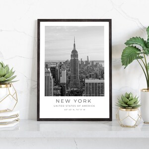 May include: Black and white photograph of the New York City skyline with the Empire State Building in the centre. The text "NEW YORK" is below the image, along with "UNITED STATES OF AMERICA" and the coordinates "40&deg; 43' N, 74&deg; 0' W".