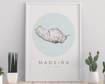 Op de afbeelding: Een witte ingelijste print met een zwart-witte kaart van Madeira, Portugal. De kaart is omgeven door een lichtblauwe cirkel. De tekst "MADEIRA" staat in zwart onder de kaart, met "PORTUGAL" in kleinere zwarte tekst eronder. De coördinaten "32° 45' N, 17° 0' W" staan in zwart onder "PORTUGAL".