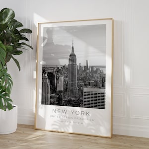 May include: Black and white photograph of the New York City skyline, featuring the Empire State Building. The image includes the text "NEW YORK", "UNITED STATES OF AMERICA", and "40&deg;43' N, 74&deg; 0' W".