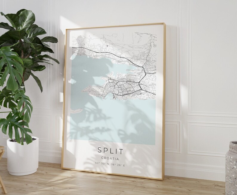 May include: A minimalist black and white map print of Split, Croatia, with a light blue background. The map is framed in a gold frame and the text "SPLIT CROATIA 43&deg; 30' N, 16&deg; 26' E" is printed below the map.