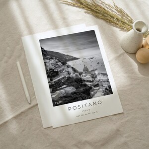 May include: Black and white photograph of Positano, Italy. The image shows a coastal town with buildings on a hillside overlooking the sea. The text "POSITANO ITALY 40&deg;38' N, 14&deg;29' E" is printed below the image.