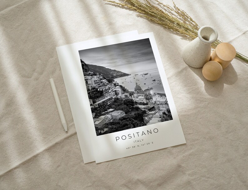 May include: Black and white photograph of Positano, Italy. The image shows a coastal town with buildings on a hillside overlooking the sea. The text "POSITANO ITALY 40&deg;38' N, 14&deg;29' E" is printed below the image.