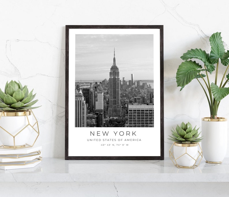 May include: Black and white photograph of the New York City skyline with the Empire State Building in the centre. The text "NEW YORK" is below the image, along with "UNITED STATES OF AMERICA" and the coordinates "40&deg; 43' N, 74&deg; 0' W".