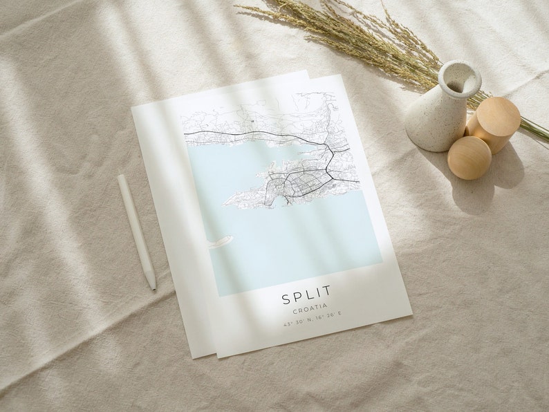 May include: A black and white map print of Split, Croatia, with the city name and coordinates printed at the bottom. The map is on a light beige fabric surface with a white vase and wooden blocks.
