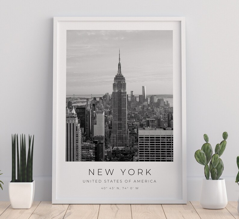 May include: Black and white photograph of the New York City skyline, featuring the Empire State Building. The text "NEW YORK" is printed below the image, along with "UNITED STATES OF AMERICA" and the coordinates "40&deg; 43' N, 74&deg; 0' W".