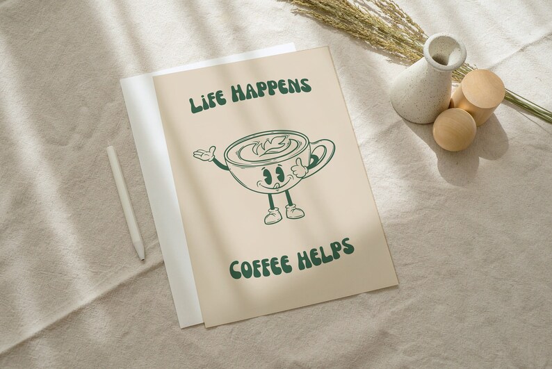 K&ouml;nnte beinhalten: Ein beiger Druck mit einer Cartoon-Kaffeetasse, auf der in dunkelgr&uuml;nen Buchstaben "Life Happens Coffee Helps" steht. Die Kaffeetasse hat Arme, Beine und ein l&auml;chelndes Gesicht. Ein wei&szlig;er Stift, eine kleine Vase und Holzkugeln sind ebenfalls im Bild.