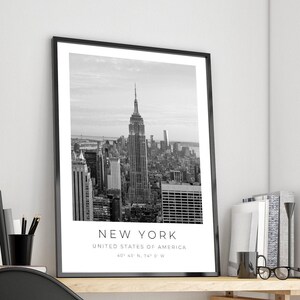 May include: Black and white photograph of the New York City skyline, featuring the Empire State Building. The image includes the text "NEW YORK", "UNITED STATES OF AMERICA", and "40&deg; 43' N, 74&deg; 0' W".
