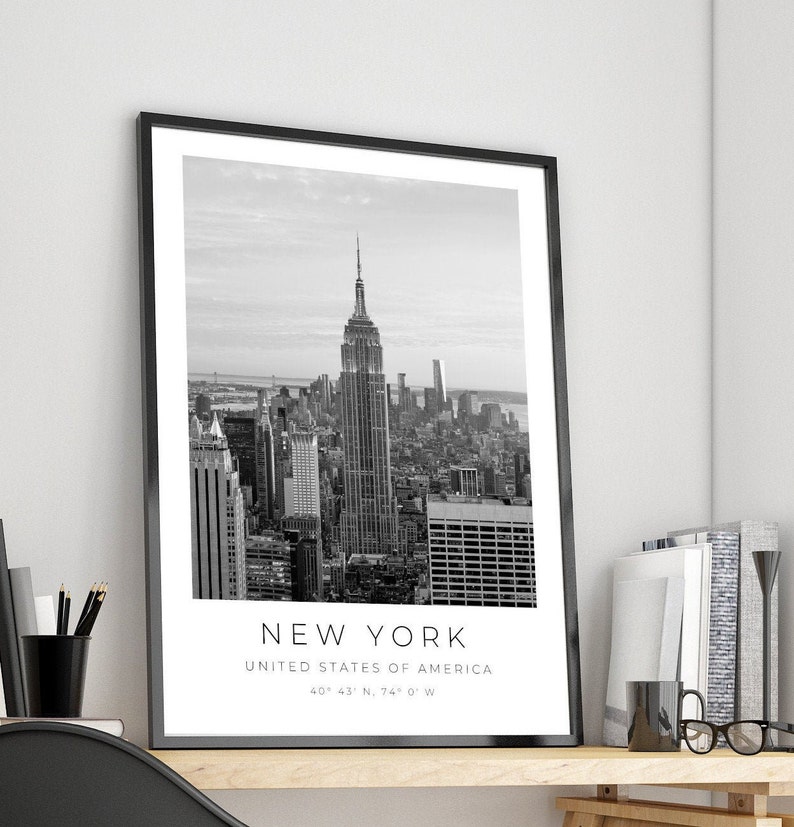 May include: Black and white photograph of the New York City skyline, featuring the Empire State Building. The image includes the text "NEW YORK", "UNITED STATES OF AMERICA", and "40&deg; 43' N, 74&deg; 0' W".