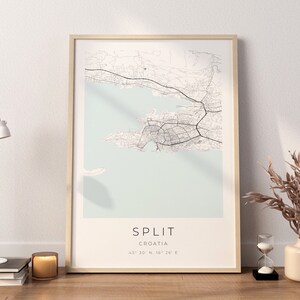 May include: A framed map print of Split, Croatia, with a light blue background and black lines showing the city streets. The text "SPLIT" and "CROATIA" are printed below the map, along with the coordinates "43&deg; 30' 10" N, 16&deg; 26' 26" E".