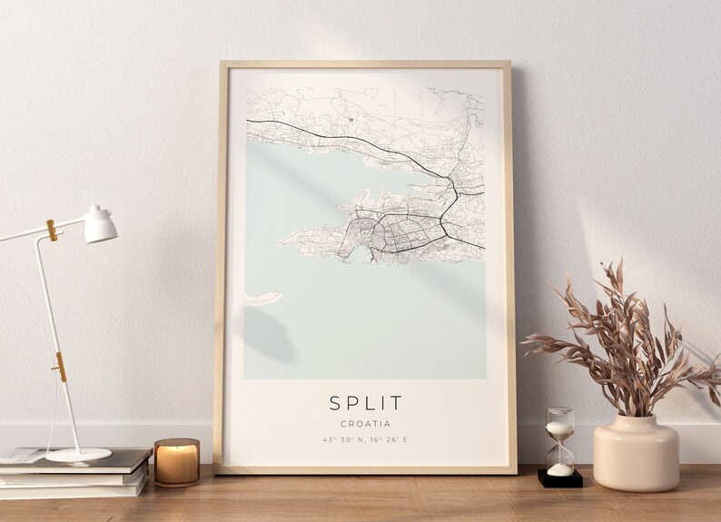 May include: A framed map print of Split, Croatia, with a light blue background and black lines showing the city streets. The text "SPLIT" and "CROATIA" are printed below the map, along with the coordinates "43&deg; 30' 10" N, 16&deg; 26' 26" E".