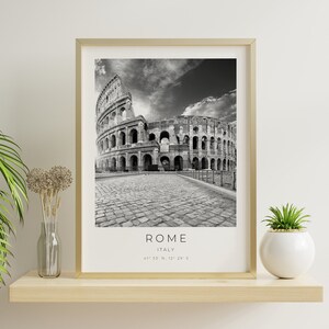 May include: Black and white photograph of the Colosseum in Rome, Italy. The photo is framed in a gold frame and is hanging on a white wall. The text "ROME, ITALY, 41&deg;53' N, 12&deg;29' E" is printed below the image.