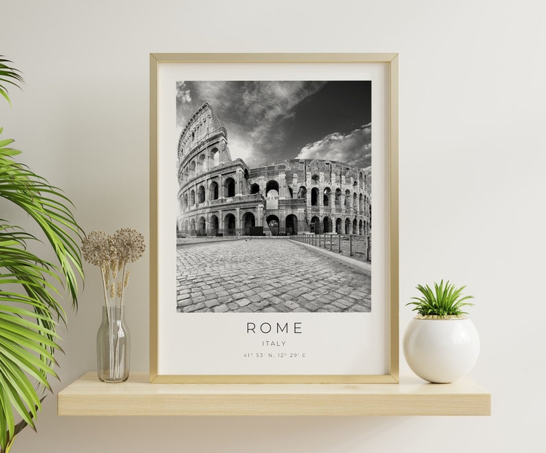 May include: Black and white photograph of the Colosseum in Rome, Italy. The photo is framed in a gold frame and is hanging on a white wall. The text "ROME, ITALY, 41&deg;53' N, 12&deg;29' E" is printed below the image.