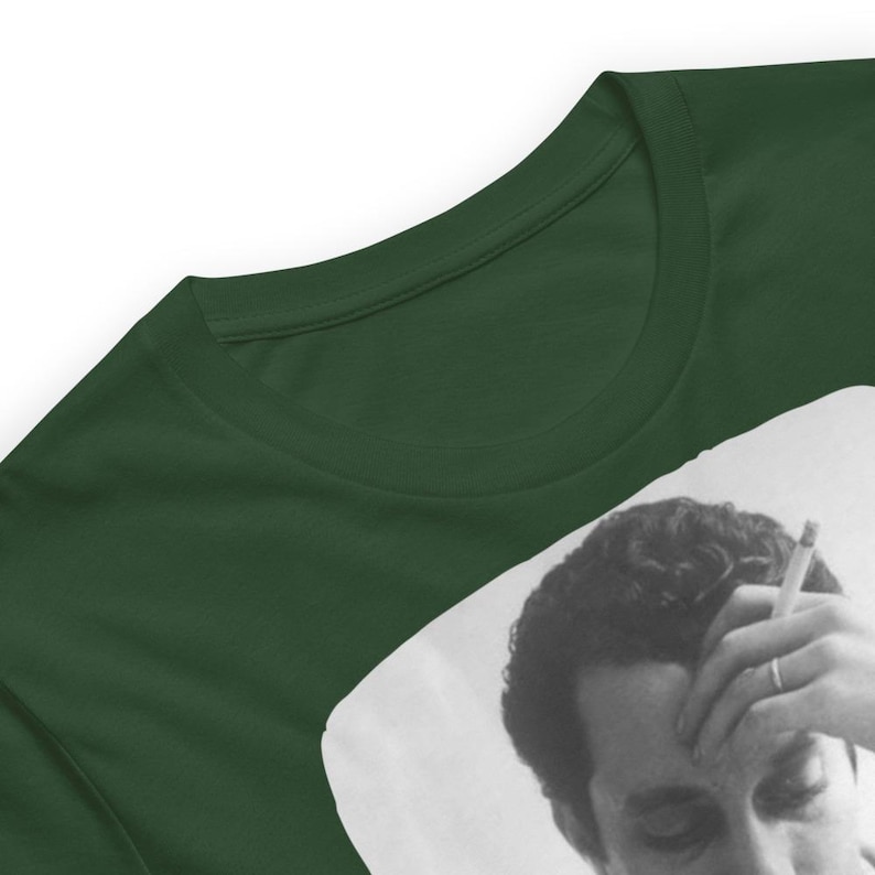 May include: A dark green t-shirt with a black and white image of a man with a cigarette in his hand. The man is looking down and has a serious expression on his face.