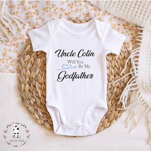 May include: White baby onesie with black text that reads "Uncle Colin Will You Be My Godfather" with a blue heart and arrow graphic.