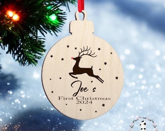 May include: A wooden Christmas ornament with a red ribbon. The ornament features a reindeer silhouette, stars, and the text "Joe's First Christmas 2024". The ornament is round with a light wood finish.